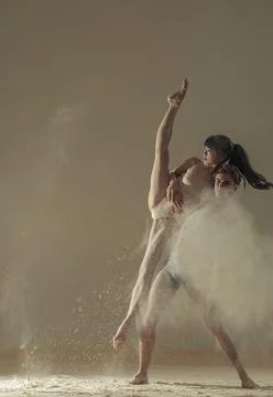 Two ballet dancers perform dance against background of white flour cloud in a Stock Photos