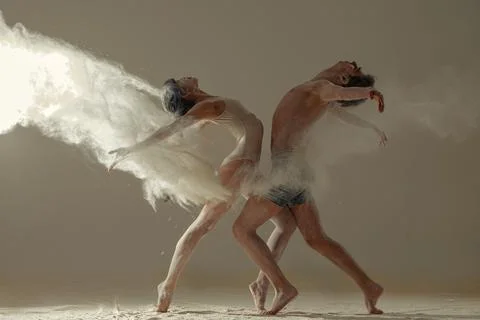 Two ballet dancers perform dance against background of white flour cloud in a Stock Photos