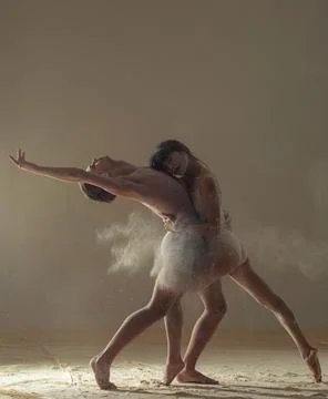 Two ballet dancers perform dance against background of white flour cloud in a Stock Photos