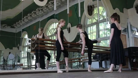 Two ballet dancers warm-up their legs and hand with their teacher Stock Footage 76650133