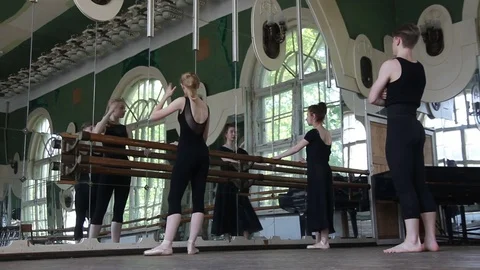 Two ballet dancers warm-up their legs and hands with their teacher Stock Footage 76651420