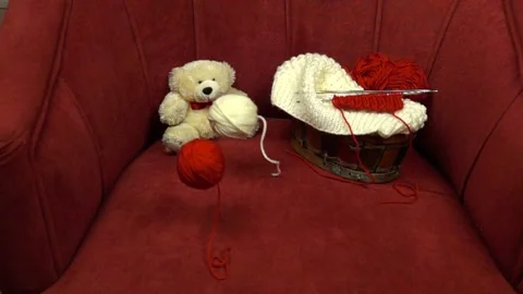 Two balls of knitting thread roll across a red velour armchair Stock Footage 270489855