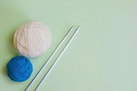 Two balls of woolen thread and long metal needles on a light green background Stock Photos