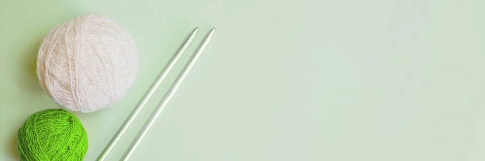 Two balls of woolen thread and long metal needles on a light green background Stock Photos