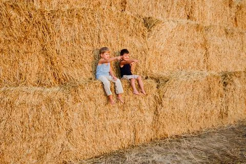 Two barefoot boy sitting on the large yellow haystacks Stock Photos