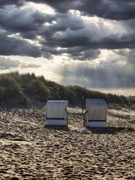 Two beach chairs in front of a dune in autumn sun rays through cloud cover Foto stock
