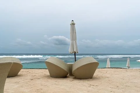Two beach chairs with small table and closed umbrella stand on empty shore by Stock Photos