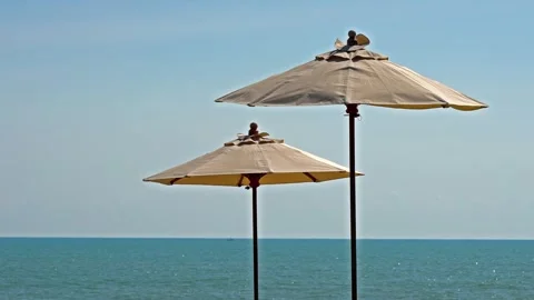 Two beach umbrellas stand against blue sky and ocean background, providing .. Stock Footage 337410509