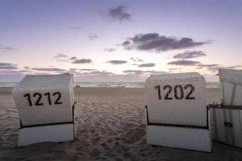  Two beachchairs on a sandy beach from behind under a light violett sky. T... Stock-Fotos