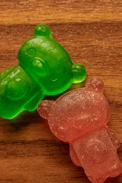 Two bears, one green and one pink, are sitting on a wooden surface Stock Photos