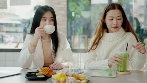 Two beautiful Asian female friends are sitting happily eating and chatting Stock Footage 167655341