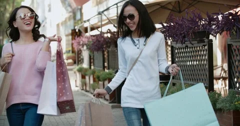 Two beautiful Asian girls have fun walking down the street with their purchases Stock Footage
