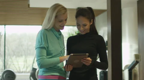 Two beautiful athletic women are using a tablet next to treadmills in sport gym Stock Footage