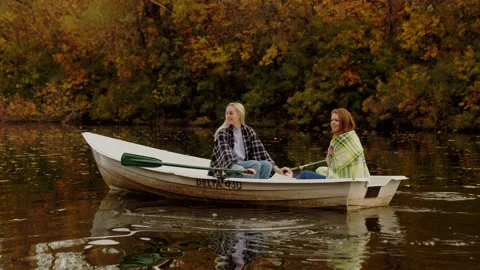 Two beautiful blond and ginger women sits in a boat on a lake in a fairy autumn Vídeos de archivo 143043661