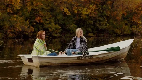 Two beautiful blond and ginger women sits in a boat on a lake in a fairy autumn Vídeos de archivo 143647200