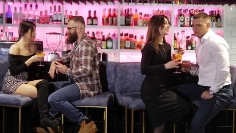Two beautiful couples are sitting in a bar, talking and drinking alcoholic Stock Footage 168620491