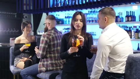 Two beautiful couples are sitting in a bar, talking and drinking alcoholic Stock Footage 168621967