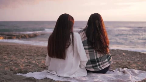 Two beautiful dark-haired women sit on a blanket and watch the sunset in the sea Stock Footage 229234763