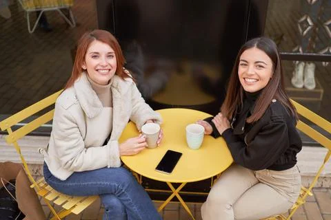 Two beautiful friends posing for the camera while holding a cup of coffee at a 스톡 사진