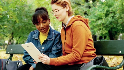 Two beautiful girlfriends sitting with tablet in autumn park, 4K Stock Footage 144616700