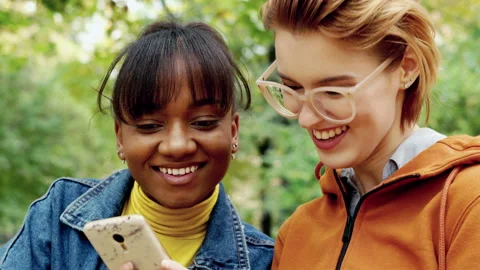 Two beautiful girlfriends using smartphone in autumn park, 4K Stock Footage 144621737