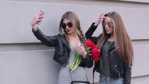 Two beautiful girls standing near the wall doing a selfie on a mobile phone Stock Footage 75002653