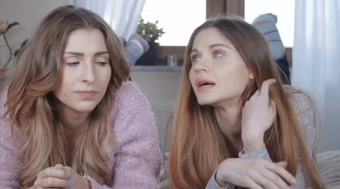 Two beautiful girls talking while lying on bed. Stockbeeldmateriaal 62340189