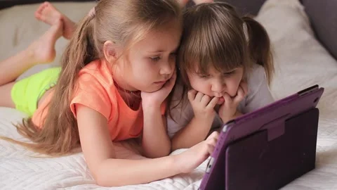 Two beautiful little sisters lying in the bed and look at the screen of a tablet Stock Footage 170956272
