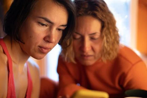 Two beautiful middle-aged smiling women look at the smartphone. A blonde woma Stock Photos
