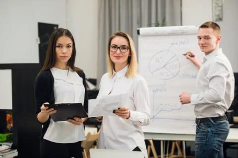 Two beautiful office workers having conversation while man colleague drawing Stock Photos