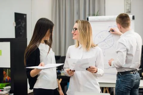 Two beautiful office workers having conversation while man colleague drawing Stock Photos