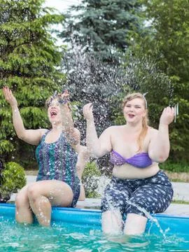 Two beautiful plus size model splashing in the pool outdoors. Stock Photos