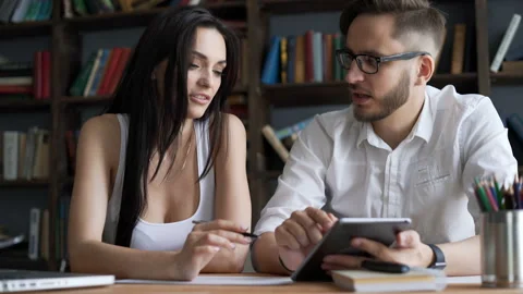 Two beautiful smart 20s students close up speak in campus library use portable d Stock Footage 199491492
