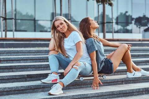 Two beautiful young girlfriends sitting on skateboard at steps on a background Stockfoto's