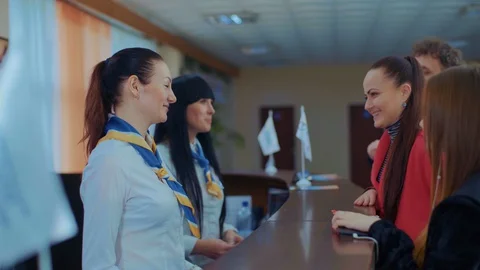 Two beautiful young stylish receptionists at a reception desk,talking to a young Stock Footage 129521845