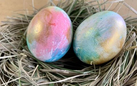 Two beautifully painted Easter eggs with vibrant colors rest in a straw nest, Stock Photos
