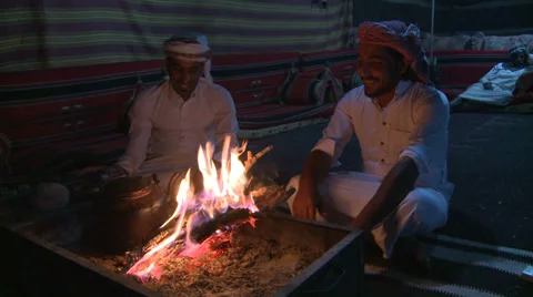 Two Bedouin men sit in a tent in front of a campfire in the desert and laugh and Video stock 34416946