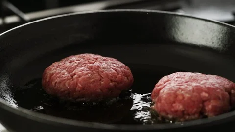 Two Beef patty's gently sizzling in a hot cast iron pan, two in frame.  Stock Footage 92149661