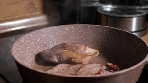 Two beef steaks are fried in a pan steam rises in slow motion Stock Footage 147932132