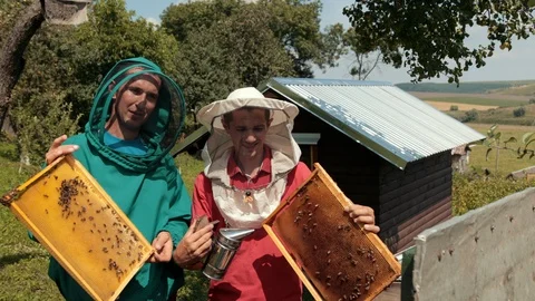 Two beekeepers in green and red special attire, collecting honey 스톡 동영상 116044842