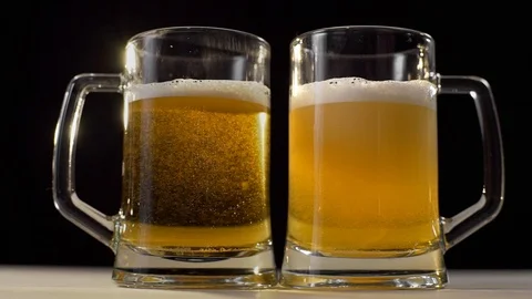 Two beer glasses are poured with foamy golden light beer on black background Stock Footage 104798366