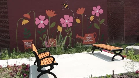 Two benches facing each other on pavement cement with pink flower mural on brick Stock Footage 247144382