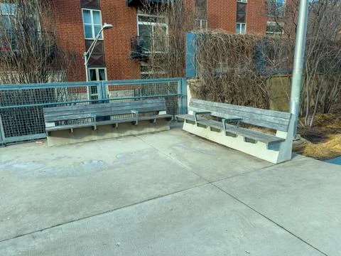 Two benches sit on a concrete platform next to a building in an urban area .. Stock Photos