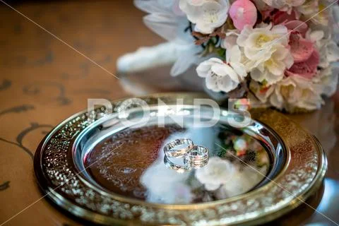 Two bicolor wedding rings on a tray with flowers in the background Stock Photos
