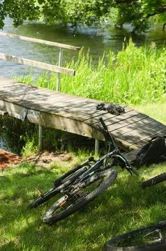 Two bicycles are lying on the grass near the pier on the lake Stock Photos