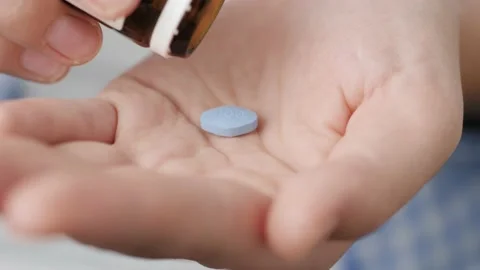 Two big blue diamond-shaped pills labeled 100 fall into palm of hand from pill Video stock 147186309