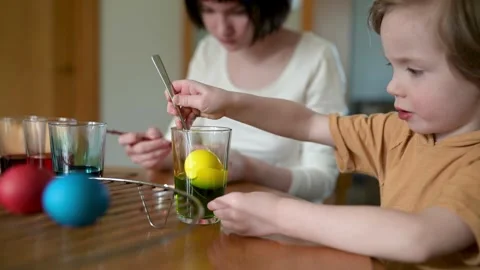Two big sisters and their little brother dyeing Easter eggs at home. Slow motion 스톡 동영상 306610947