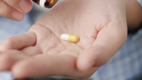 Two big white-yellow cylindrical capsule pills fall into palm of hand from pill Stockbeeldmateriaal 147188170
