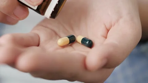 Two big yellow-green cylindrical capsule pills fall into palm of hand from pill Stock-Footage 147186775