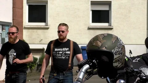 Two bikers with beards walking by motorcycle with helmet at biker party Stock Footage 90440452